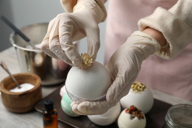 Photo of Woman in gloves decorating bath bomb with flower at table, closeup