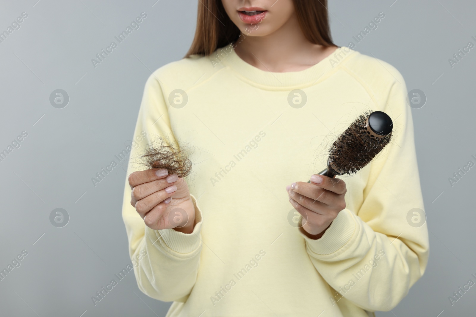 Photo of Woman holding brush with lost hair on light grey background, closeup. Alopecia problem