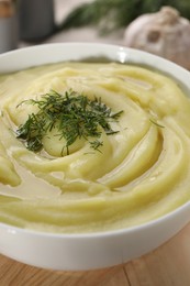 Photo of Bowl of tasty cream soup with dill on wooden table, closeup