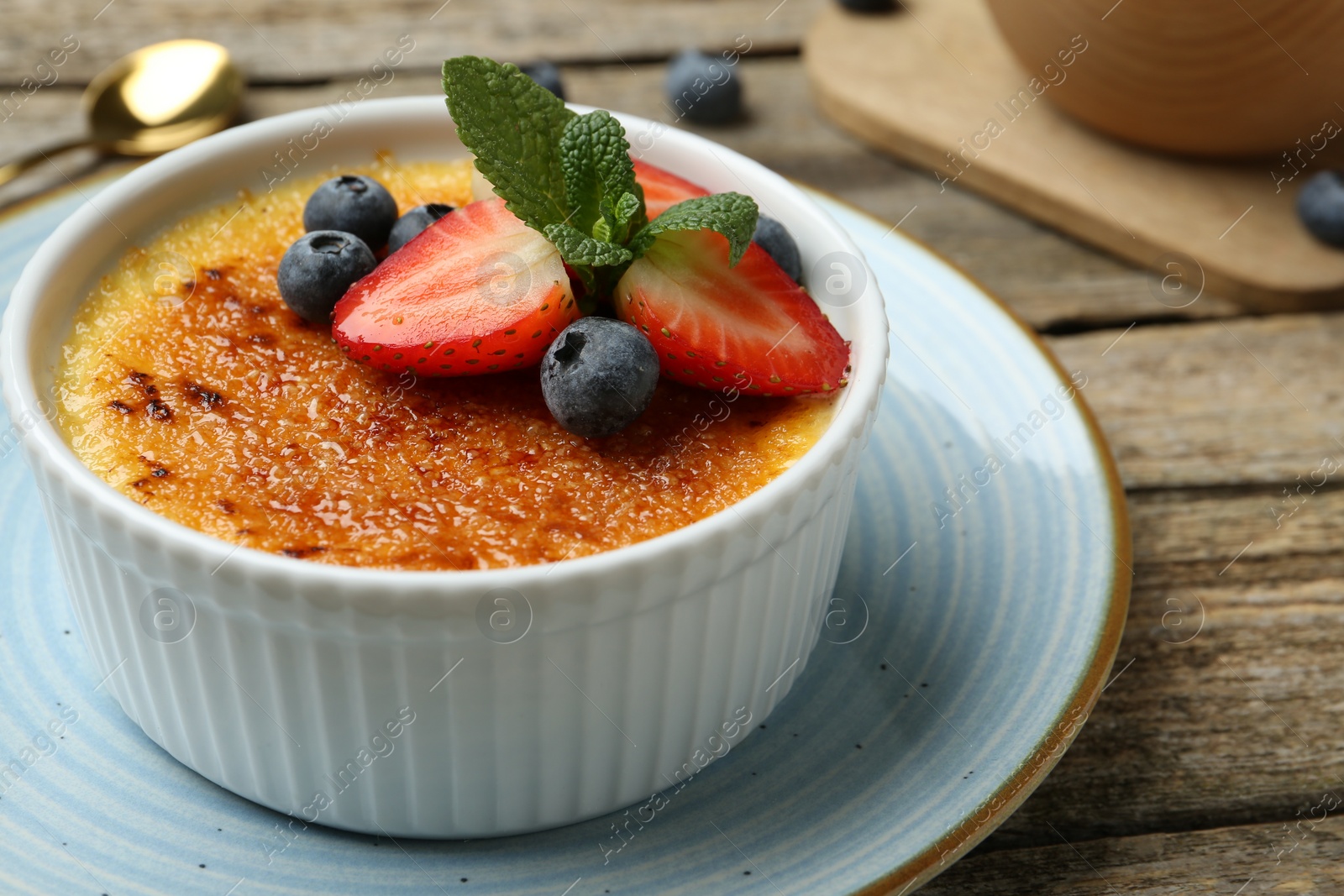 Photo of Delicious creme brulee with berries and mint in bowl on wooden table, closeup