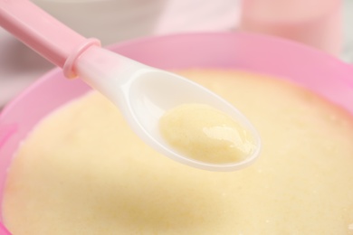 Spoon of healthy baby food over bowl, closeup