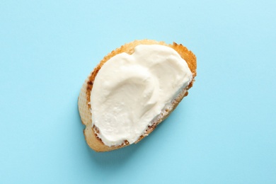 Piece of baguette with tasty cream cheese on color background, top view