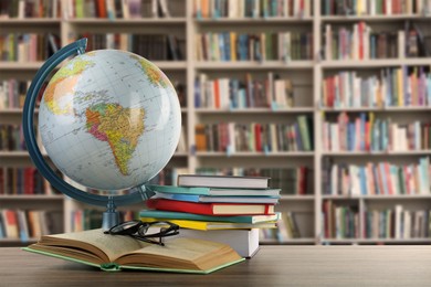 Image of Globe, books and eyeglasses on wooden table on wooden table in library. Space for text