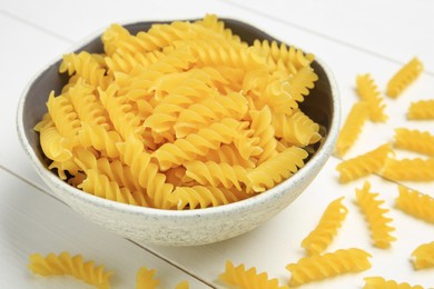 Photo of Raw fusilli pasta in bowl on white wooden table, closeup