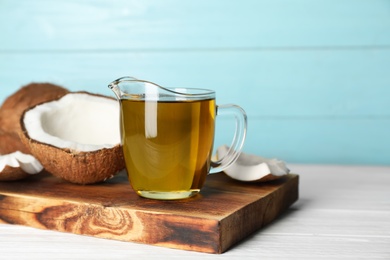 Photo of Ripe coconut and oil in pitcher on wooden table. Healthy cooking