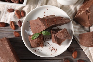 Photo of Pieces of tasty milk chocolate, cocoa beans, powder and mint on wooden table, flat lay