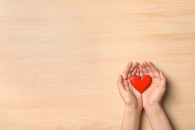 Photo of Woman holding heart on wooden background, top view with space for text. Donation concept