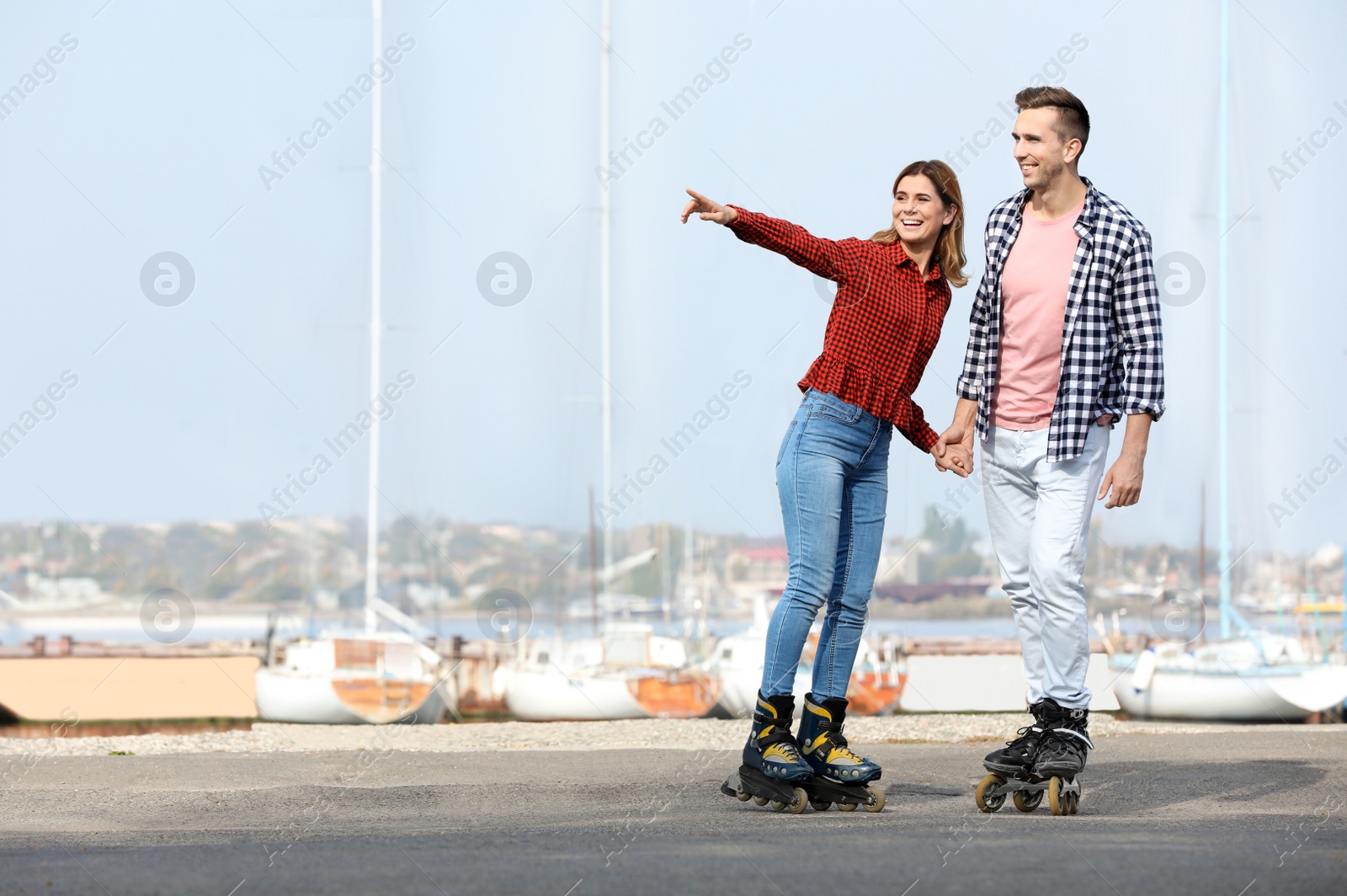 Photo of Happy lovely couple roller skating on embankment. Space for text