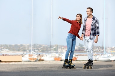 Happy lovely couple roller skating on embankment. Space for text