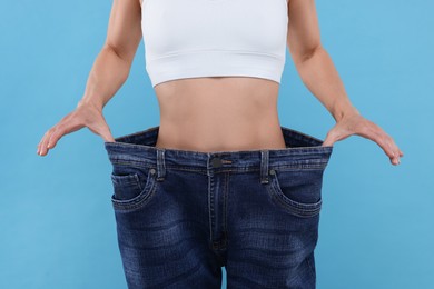Photo of Slim woman wearing big jeans on light blue background, closeup. Weight loss