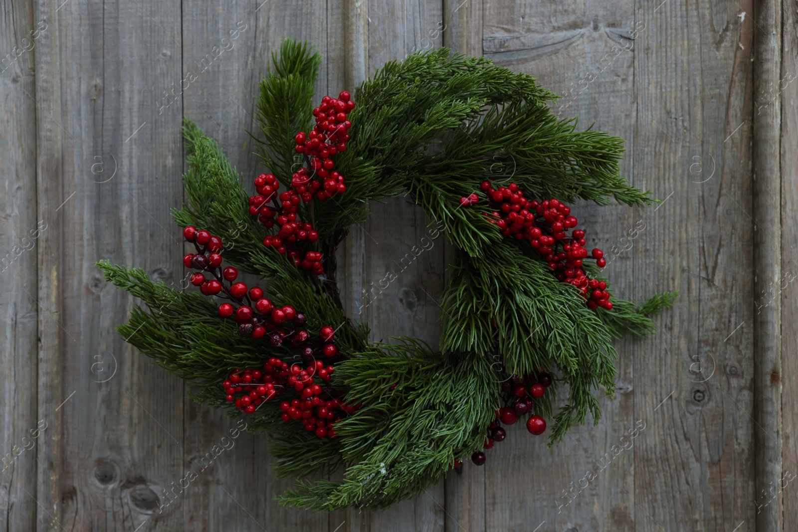 Photo of Beautiful Christmas wreath with red berries hanging on wooden wall