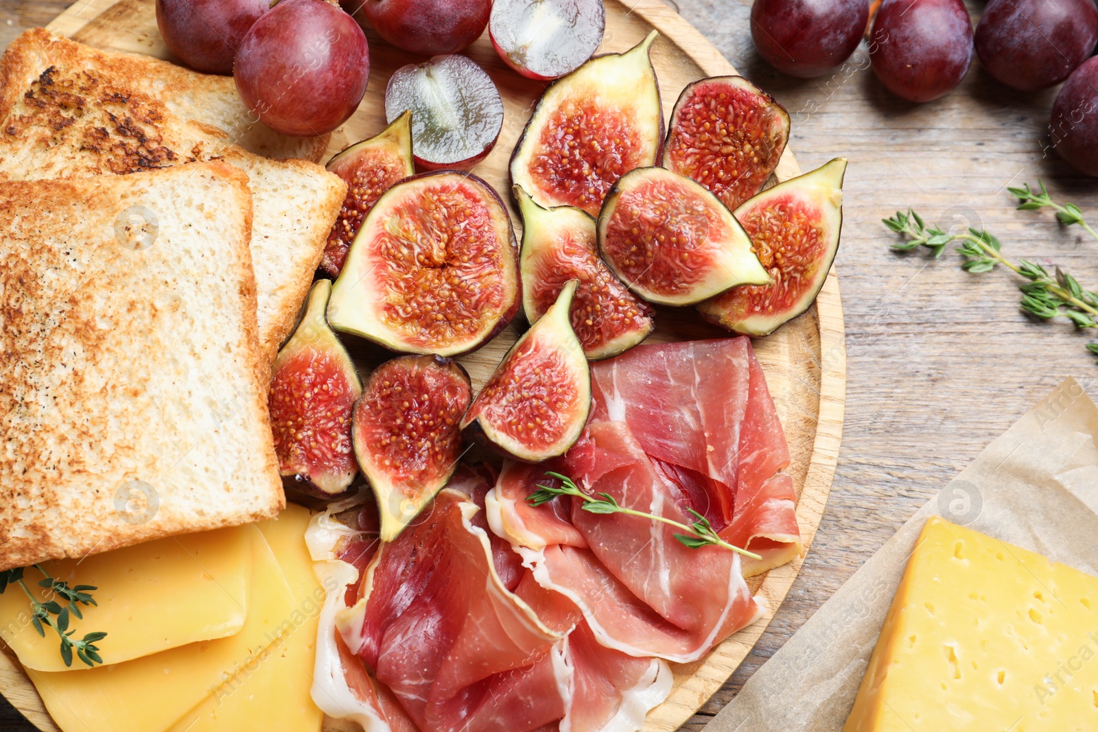 Photo of Delicious ripe figs, prosciutto and cheese served on wooden table, flat lay