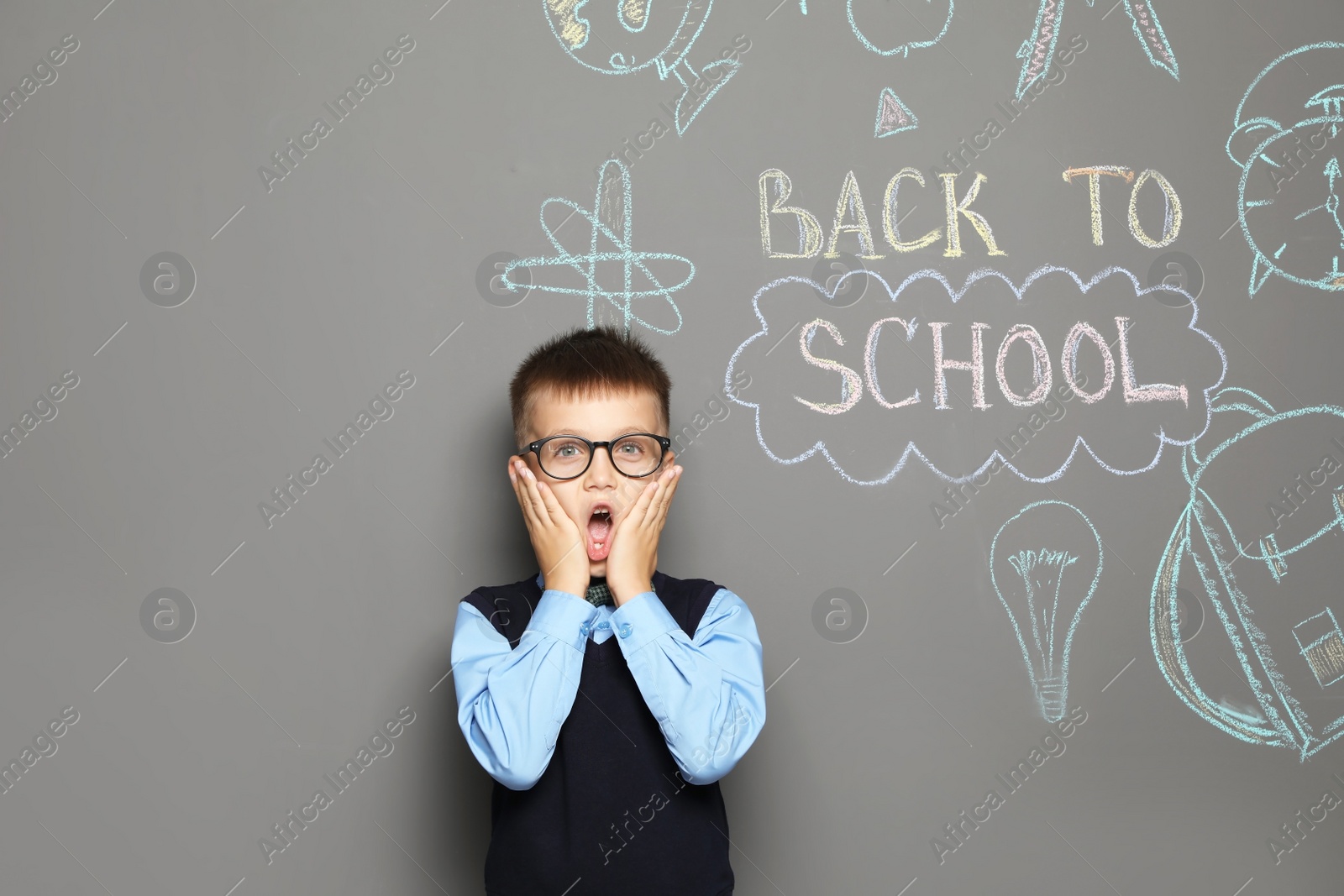 Photo of Little child in uniform near drawings with text BACK TO SCHOOL on grey background