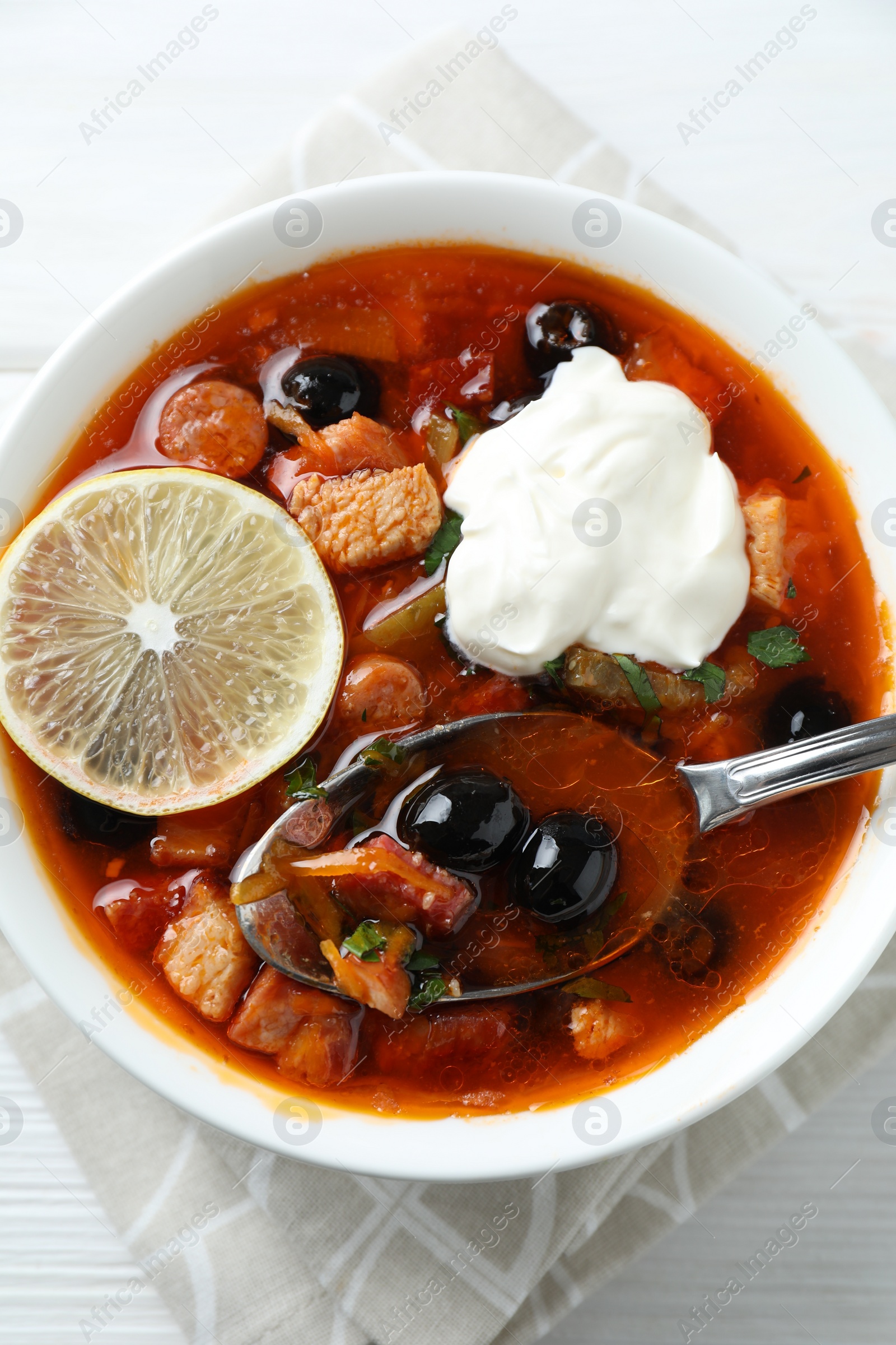 Photo of Meat solyanka soup with sausages, olives, vegetables and spoon on white table, top view