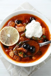 Meat solyanka soup with sausages, olives, vegetables and spoon on white table, top view