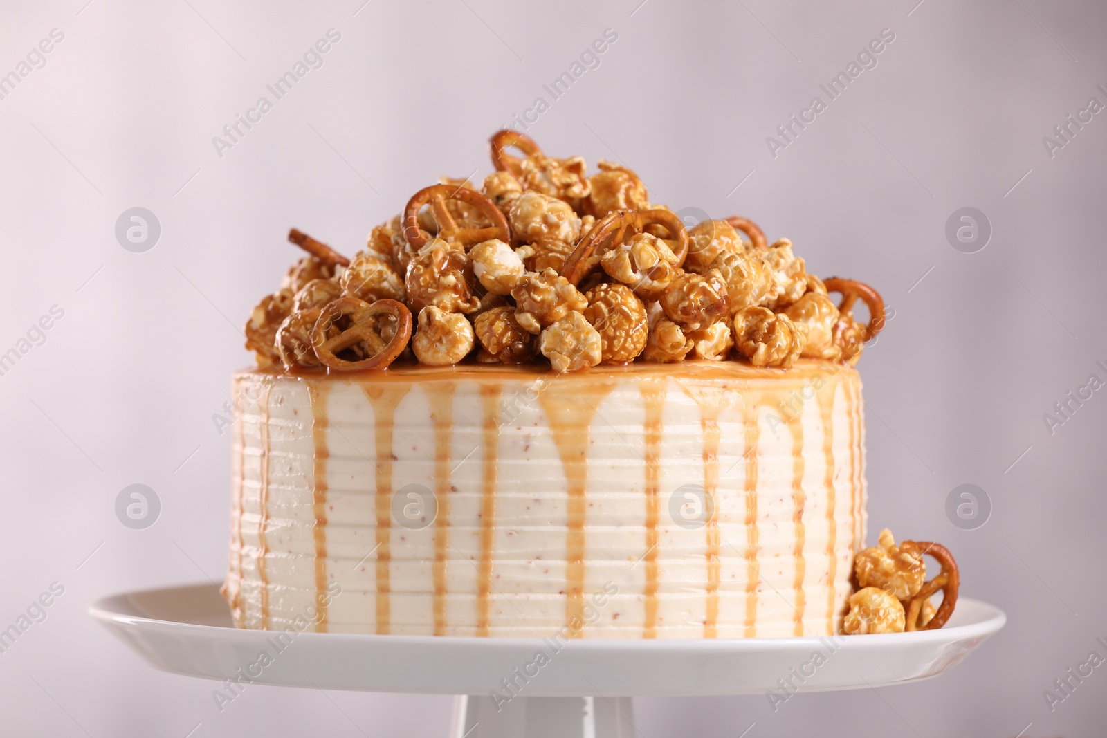 Photo of Caramel drip cake decorated with popcorn and pretzels on light background, closeup