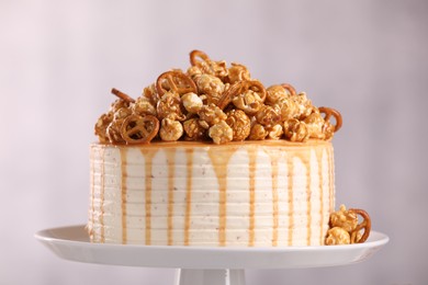 Photo of Caramel drip cake decorated with popcorn and pretzels on light background, closeup