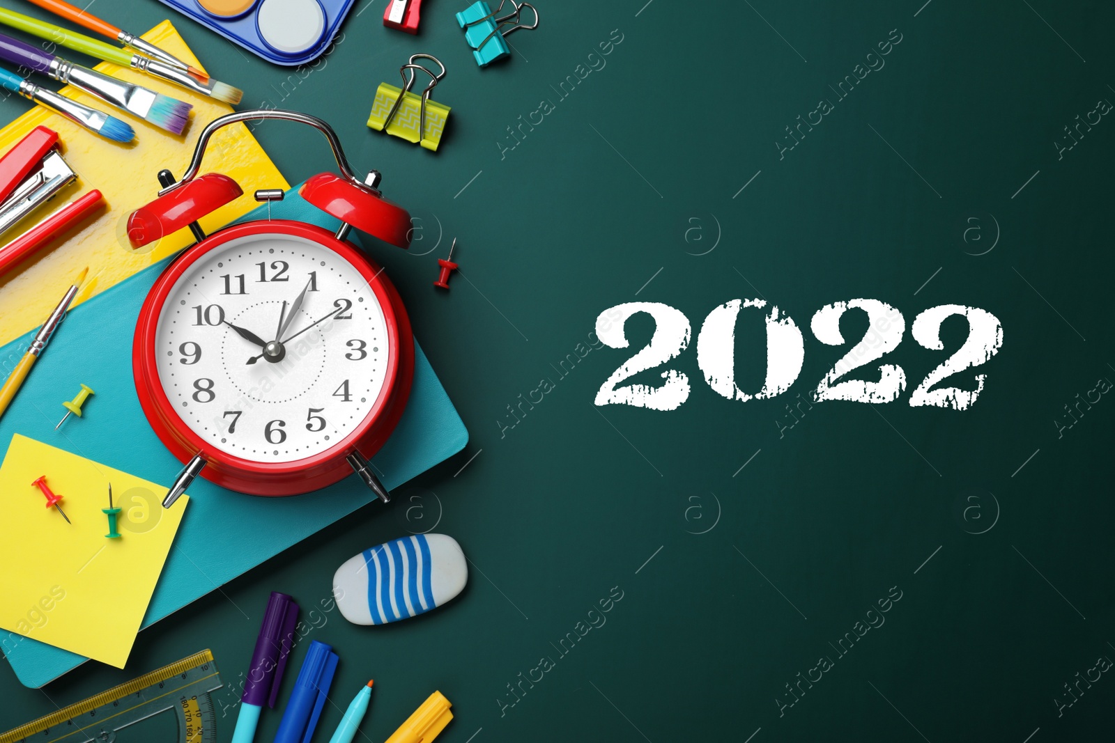 Image of Back to school 2022. Flat lay composition with alarm clock and different stationery on green chalkboard