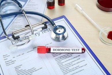 Photo of Hormone test. Sample tube with blood, stethoscope and laboratory form on table, above view