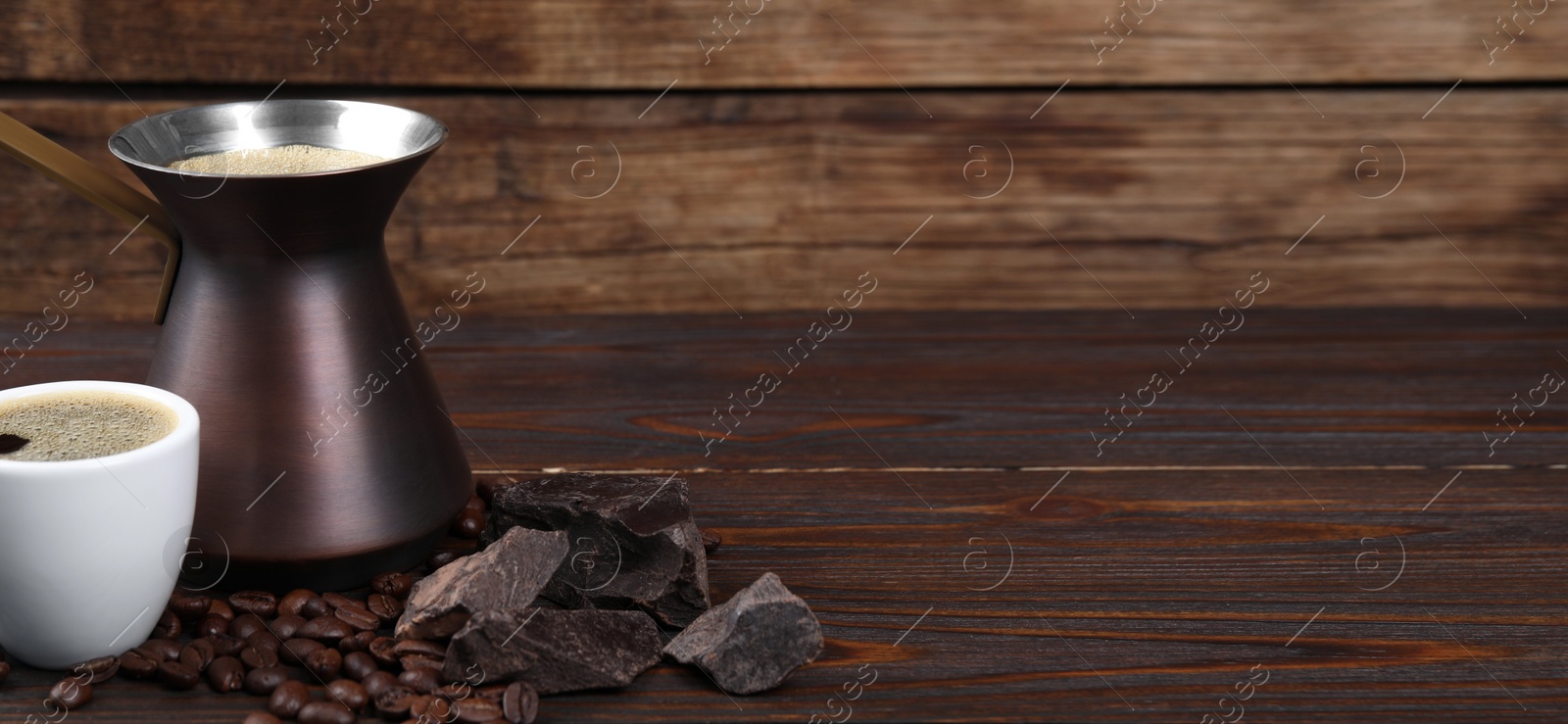 Image of Turkish coffee. Cezve and cup with freshly brewed beverage, coffee beans and chocolate on wooden table. Banner design with space for text