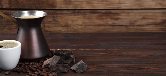 Image of Turkish coffee. Cezve and cup with freshly brewed beverage, coffee beans and chocolate on wooden table. Banner design with space for text