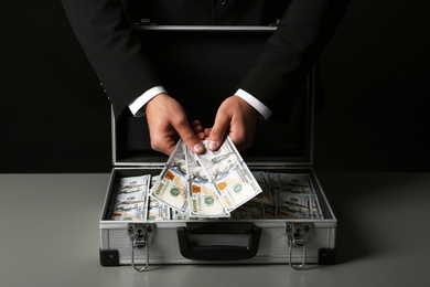 Businessman with suitcase full of money on dark background