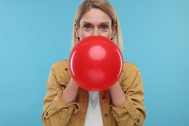 Photo of Woman blowing up balloon on light blue background