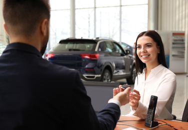 Photo of Salesman giving key to client in car dealership