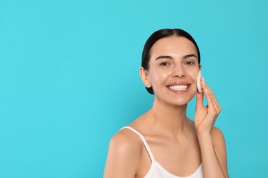 Photo of Young woman using cotton pad with micellar water on light blue background, space for text