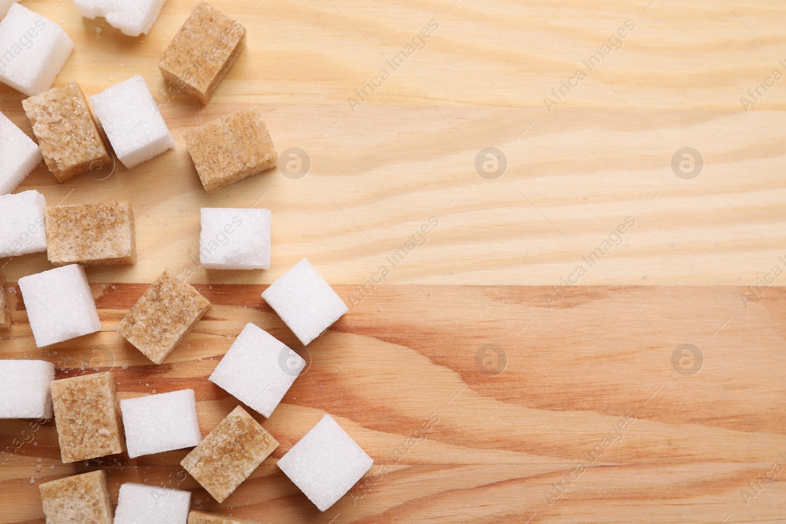 Photo of White and brown sugar cubes on wooden table, flat lay. Space for text