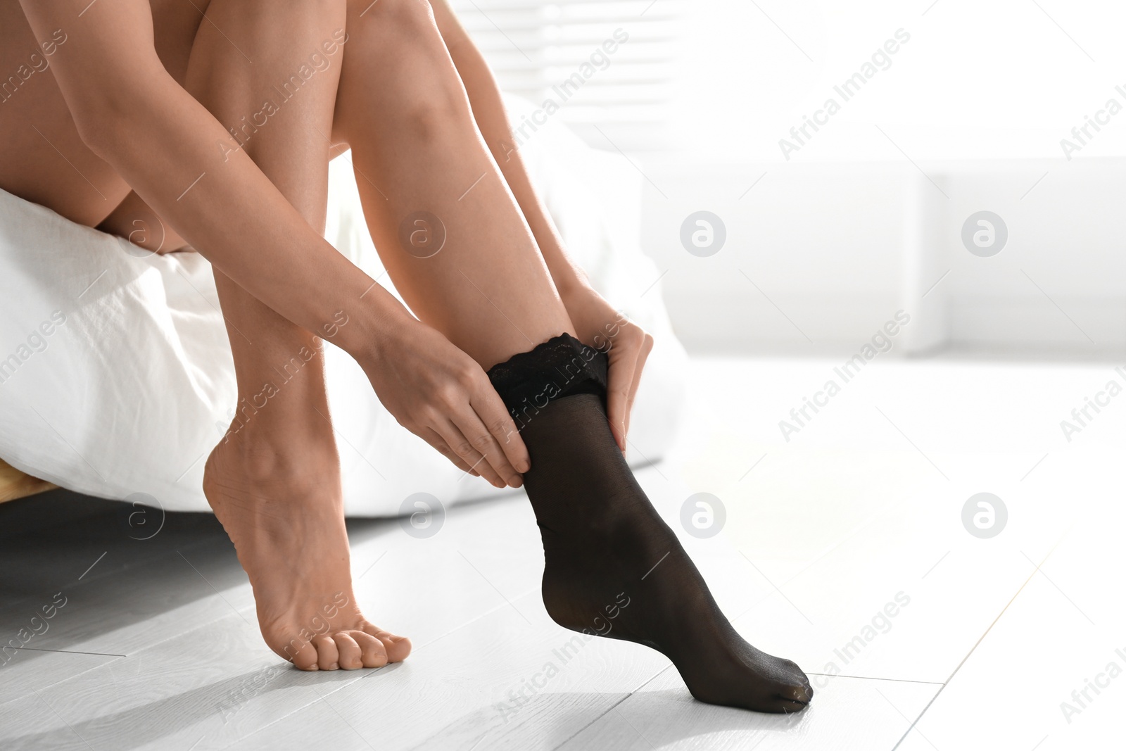 Photo of Young woman putting on stocking in bedroom, closeup