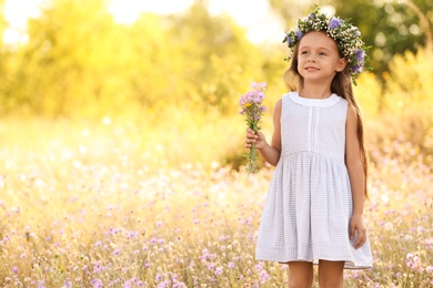 Cute little girl wearing beautiful wreath with bouquet of wildflowers outdoors, space for text. Child spending time in nature