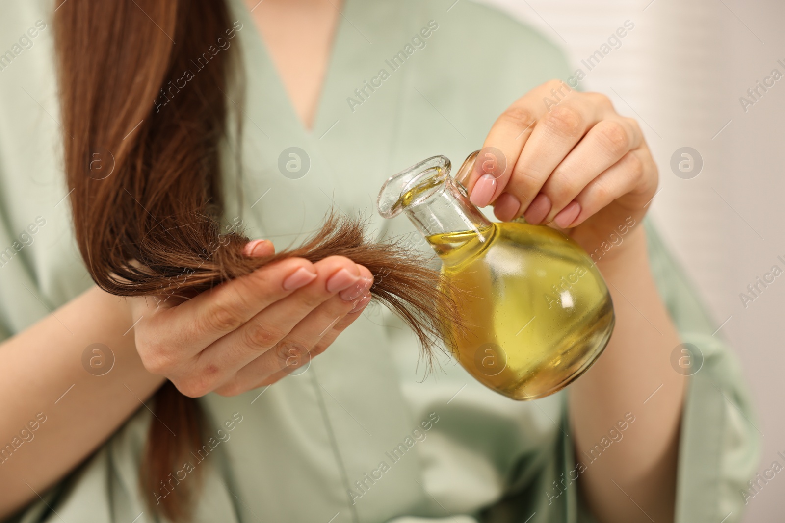 Photo of Woman applying oil hair mask onto ends at home, closeup