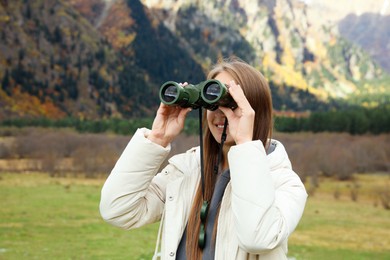 Woman looking through binoculars in beautiful mountains