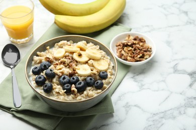 Tasty oatmeal with banana, blueberries, walnuts and milk served in bowl on white marble table, space for text