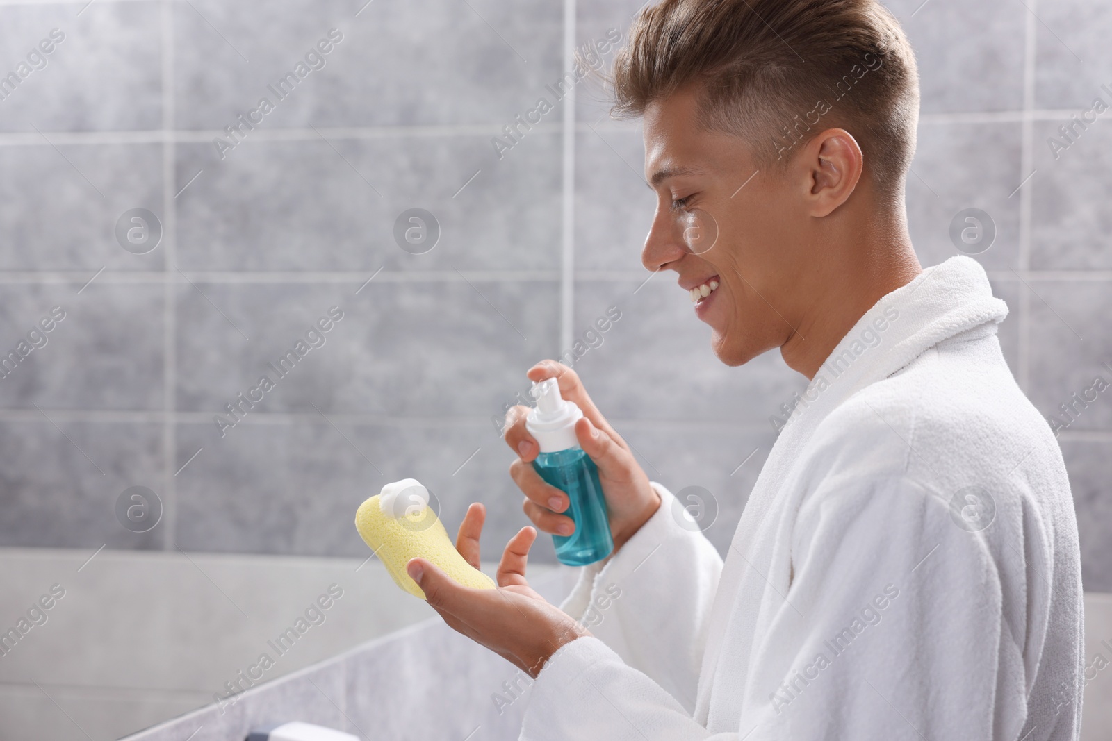 Photo of Happy young man applying face cleanser on sponge in bathroom. Space for text