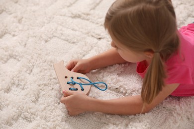 Photo of Little girl playing with wooden lacing toy on carpet indoors