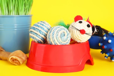 Photo of Various pet toys, bowl and wheatgrass on yellow background, closeup