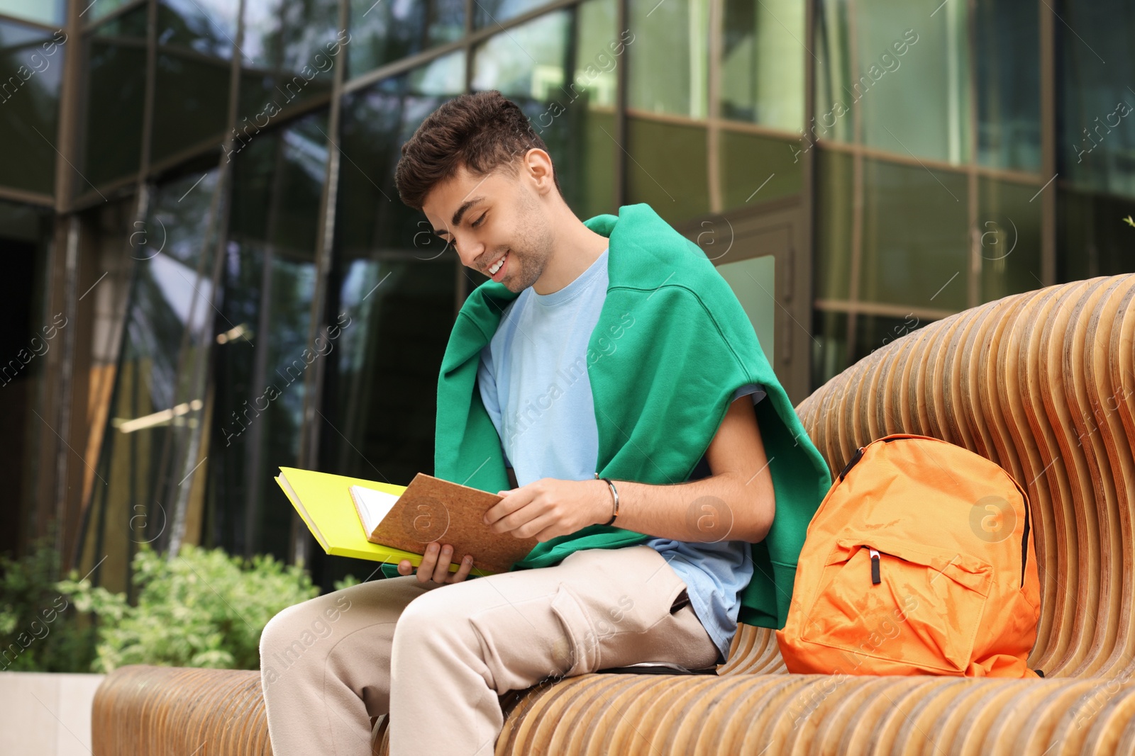 Photo of Happy young student studying with notebooks on bench outdoors