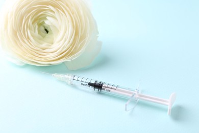 Cosmetology. Medical syringe and ranunculus flower on light blue background