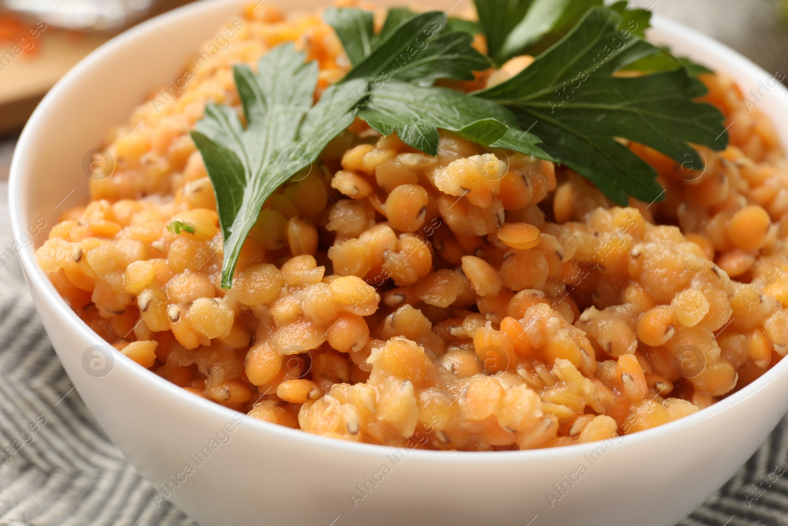 Photo of Delicious red lentils with parsley in bowl on table, closeup