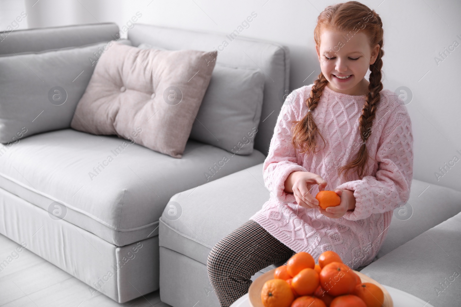 Photo of Happy girl peeling ripe tangerine on sofa at home