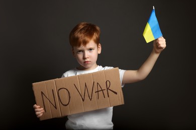 Photo of Boy holding poster No War and Ukrainian flag against black background