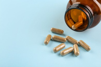 Photo of Bottle and vitamin capsules on light blue background, closeup. Space for text