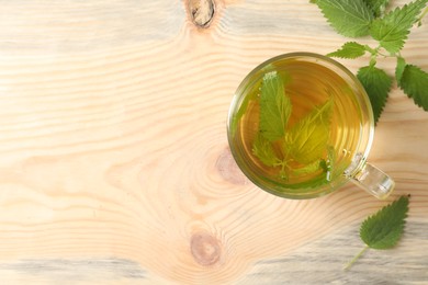 Photo of Glass cup of aromatic nettle tea and green leaves on wooden table, flat lay. Space for text