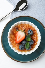 Photo of Delicious creme brulee with berries and mint in bowl on white wooden table, top view