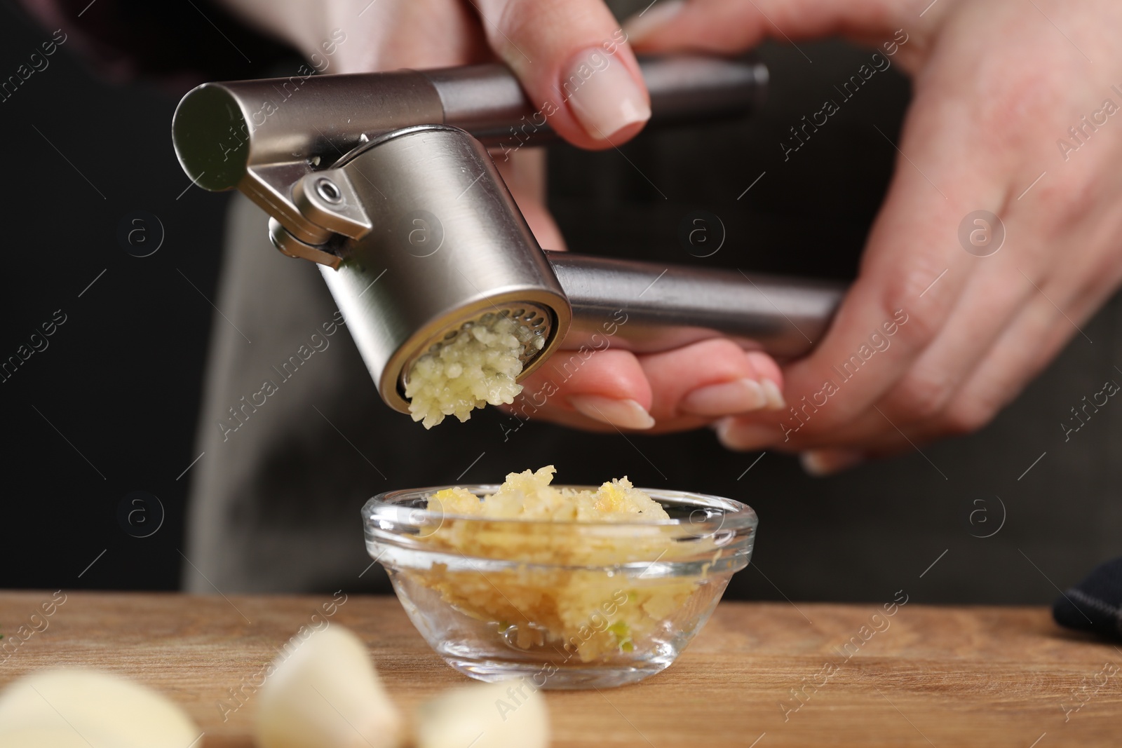 Photo of Woman squeezing garlic with press at wooden table, closeup