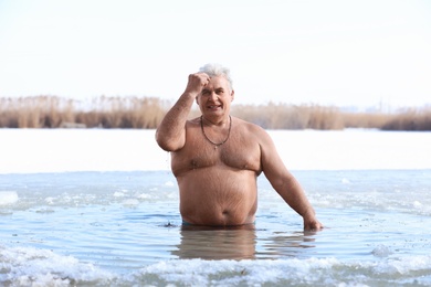 Photo of Mature man immersing in river on winter day. Baptism ritual