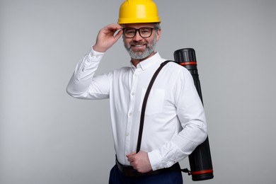 Photo of Architect in hard hat with drawing tube on grey background