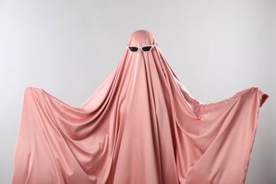 Photo of Glamorous ghost. Woman in pink sheet with sunglasses on light grey background